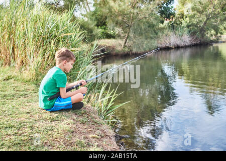 Jeune, garçon âgé de 6 ans, assis avec des jambes croisées pêche de la rive d'un étang dans Queensland Australie. Banque D'Images