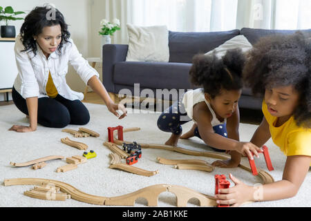 Maman et les enfants dans la salle de séjour des enfants qui jouent ensemble à dessin plancher tandis que jeune mère de détente à la maison sur le canapé, petite fille s'amusant Banque D'Images