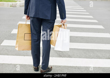 Man with shopping bags debout au début de passage pour piétons, vue de l'arrière Banque D'Images