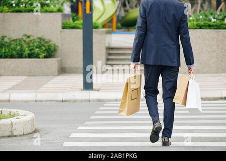 Vue arrière du businessman crossing road avec de nombreux sacs de magasinage dans les mains Banque D'Images