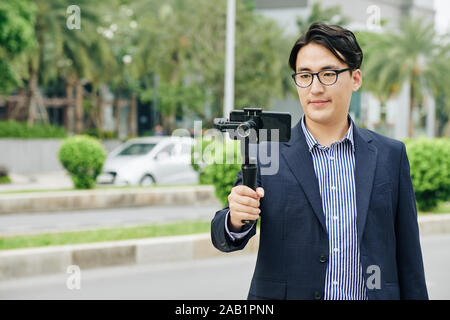 L'homme asiatique dans les verres faire video sur smartphone connecté à monopod Banque D'Images
