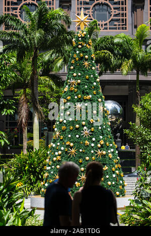 Vue verticale de deux personnes en silhouette debout devant un grand arbre de Noël avec une étoile dorée sur la pointe, Singapour, Asie du Sud-est. Banque D'Images