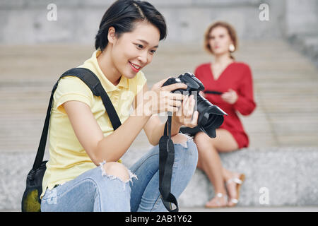 Heureux femme photographe photos sur l'écran de contrôle de l'appareil photo numérique après le tournage en extérieur modèle Banque D'Images