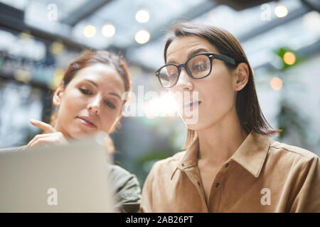 Low angle portrait of contemporary young woman using laptop in cafe tout en travaillant sur des projet d'entreprise avec collègue Banque D'Images