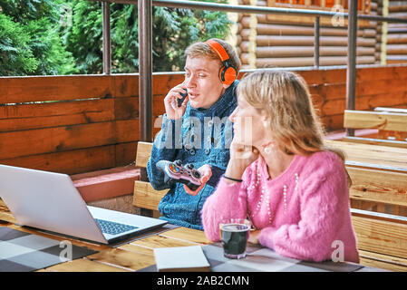 Jeune mec joue à des jeux sur un ordinateur portable dans un café à proximité. La jeune fille est en train de lire un livre. concept d'usure Banque D'Images