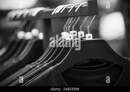 Une image noir et blanc de cintres suspendus dans le magasin, sur laquelle accrocher de simples t-shirts de différentes tailles. Banque D'Images