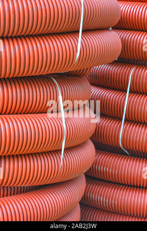 De nouvelles bobines de tuyau en plastique rouge avec des gouttes de pluie. Le tube en plastique rouge pour la protection du câble souterrain. Premier étage d'une pelote de tube ondulé rouge. Pla Banque D'Images