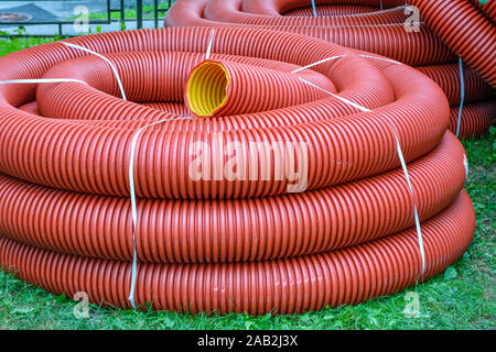 De nouvelles bobines de tuyau en plastique rouge avec des gouttes de pluie sur la ville de pelouse avec l'herbe verte. Le tube en plastique rouge pour la protection du câble souterrain. Premier étage de pelote Banque D'Images