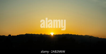 Coucher de soleil sur les montagnes. Collines couvertes d'arbres, silhouette noire contre le fond de ciel de couleur orange clair Banque D'Images