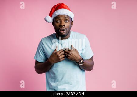 Le choc émotionnel de teint foncé lui-même, wearing Santa hat, white t shirt, avec à la bouche ouverte, ne peut pas croire en nouvelles inattendues Banque D'Images