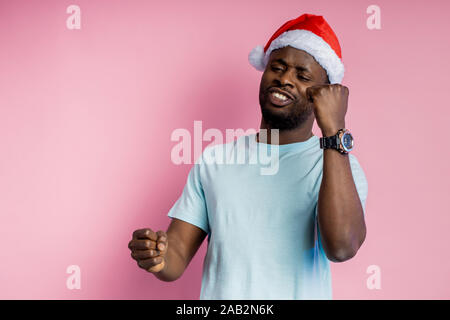 Gai homme teint foncé work, soutenir l'équipe de football, jeu de sport de l'observation, la célébration, successm wearing Santa hat,blanc t shirt, stand Banque D'Images
