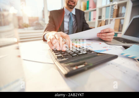 Close up of man méconnaissable le calcul des dépenses d'entreprise tandis que sitting at desk in office, focus on hand en appuyant sur les touches de la calculatrice, copy space Banque D'Images