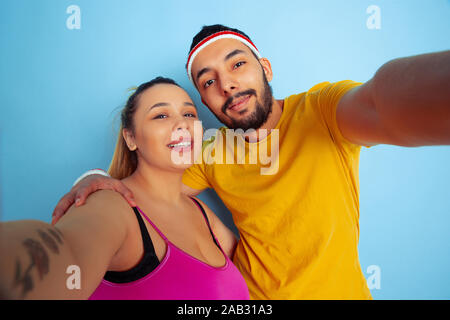 Young pretty caucasian couple dans des vêtements de la formation sur fond bleu Concept du sport, des émotions humaines, d'expression, le mode de vie sain, relation, famille. Faire ensemble et selfies hugging. Banque D'Images