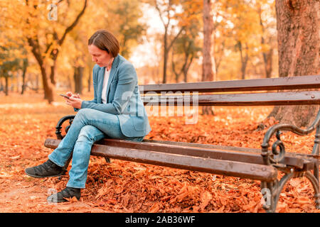 Femme saisissez du texte sur téléphone mobile sur l'automne banc de parc, avec copie espace selective focus Banque D'Images