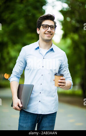 Aller à l'université étudiant Hipster avec ordinateur portable et tasse de café. Homme barbu portant des tenues élégantes marche sur la ville et de la rue Banque D'Images