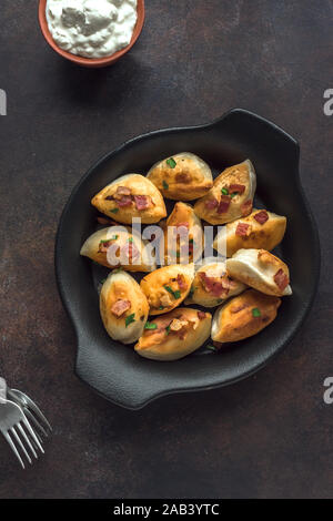 Boulettes frites farcies de viande et de pommes de terre (pierogi) saupoudré de bacon et le persil et la crème fraîche sur le tableau noir, vue du dessus, copiez l'espace. Banque D'Images