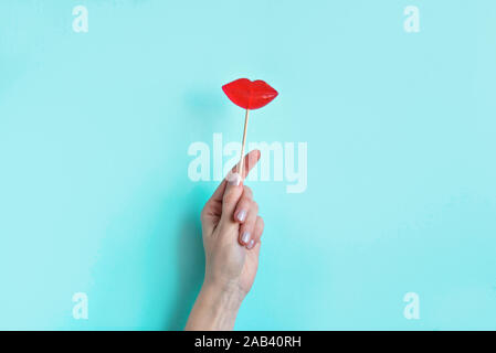 Hand holding Red Lips Lollipop. Bonbons sucettes en forme de lèvres rouges, concept minimal composition sur fond bleu, l'espace de copie. Banque D'Images