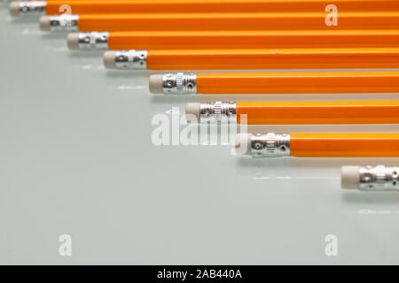 Arrière-plan avec un motif composé d'un gros plan d'une rangée de crayons de plomb blanc orange avec des caoutchoucs sur la fin est posé sur une plaque de verre blanc. Banque D'Images