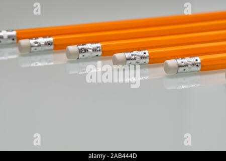 Arrière-plan avec un motif composé d'un gros plan d'une rangée de crayons de plomb blanc orange avec des caoutchoucs sur la fin est posé sur une plaque de verre blanc. Banque D'Images