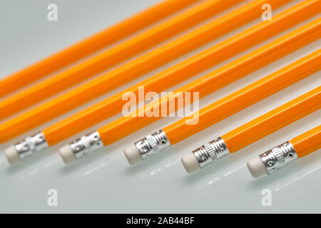 Arrière-plan avec un motif composé d'un gros plan d'une rangée de crayons de plomb blanc orange avec des caoutchoucs sur la fin est posé sur une plaque de verre blanc. Banque D'Images