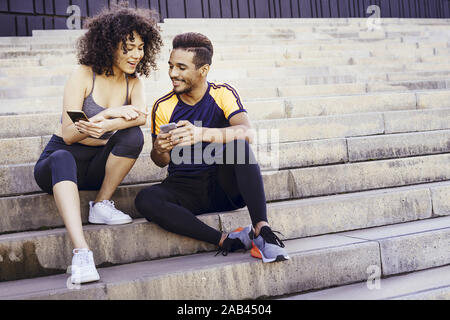 Happy young couple athlétique à l'application de sport dans leur téléphone mobile dans les escaliers lors d'un reste de l'entraînement, de la technologie dans le sport et la santé l Banque D'Images