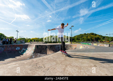 Patinage à roulettes professionnelle hors d'un bol en béton et de faire un ensemble d'astuces au skatepark local avec les gens qui regardent, les sports extrêmes Banque D'Images