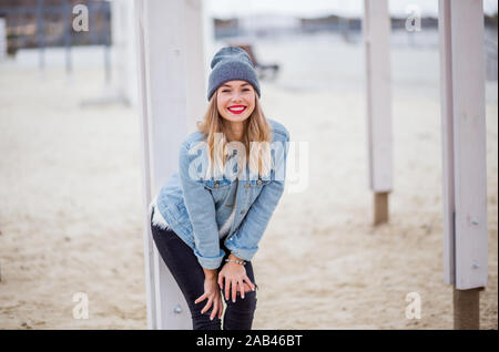 Urban style blond woman wearing hat et veste jeans avec téléphone rouge de mains, de l'espace pour le texte. Banque D'Images