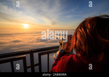 Femme assise sur le sommet de la montagne en regardant le lever du soleil sur une mer de brume Banque D'Images