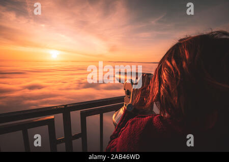 Femme assise sur le sommet de la montagne en regardant le lever du soleil sur une mer de brume Banque D'Images