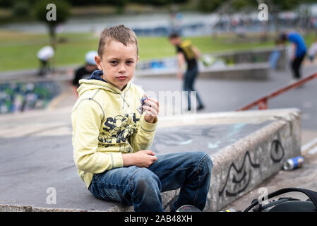 Un mignon petit garçon avec TDAH, l'autisme, du syndrome d'Asperger équitation autour du skatepark, de refroidissement et d'avoir du plaisir tout en s'exerçant et libération d'énergie Banque D'Images