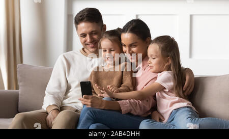 Heureux parents avec enfants filles vous détendre on sofa using smartphone Banque D'Images