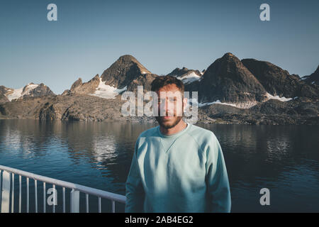 Jeune Voyageur Man with hat smiling et relaxant avec vue lac et montagne sereine voyage paysage concept randonnée vie vacances estivales Banque D'Images