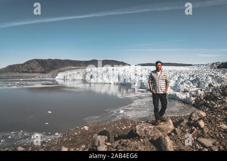 Un jeune homme traveler'debout devant Eqip Sermia appelé glacier Eqi Glacier. Mur de glace en arrière-plan. La notion de réchauffement global et Banque D'Images