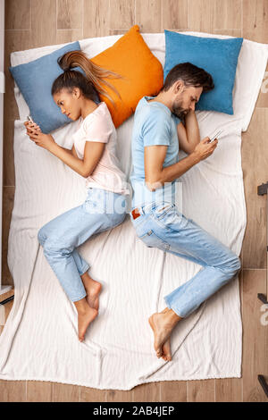 Jeunes adultes en petite amie et petit ami allongé sur bed and using smartphone Banque D'Images