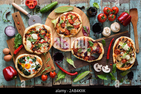 Flatlay d'une saine alimentation intérieure de style italien. Pizzas rustiques avec des légumes, de salami, les oeufs et les champignons servi avec du vin rouge sur les planches à découper en chêne Banque D'Images