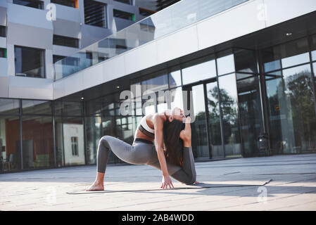 Matin d'été ensoleillé. Jeune femme athlétique doing handstand on city park street entre les bâtiments urbains modernes. L'exercice à l'extérieur de vie sain Banque D'Images