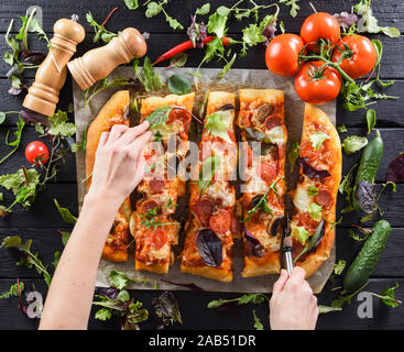 Femme svelte mains big coupe pizza aux champignons maison entouré d'herbes fraîches et légumes sur fond noir vue ci-dessus Banque D'Images