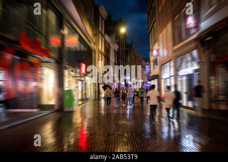 Blurry motion image de jeunes gens marchant sur la rue Kalverstraat, qui est l'une des principales rues commerçantes d'Amsterdam. Il s'agit d'une nuit d'été pluvieux. Banque D'Images