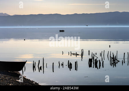 Un pêcheur de prêt dans son bateau à rames sur le lac d'Ohrid à Peshtani dans le Nord de la Macédoine, avec l'Albanie dans la distance, au nord de la Macédoine, de l'Europe. Banque D'Images