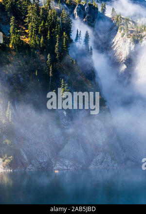 Un homme dans un petit radeau pneumatique de l'aviron sur le lac de la neige au-dessus de Snoqualmie Pass dans la partie centrale de la chaîne des Cascades dans l'État de Washington, USA. Banque D'Images