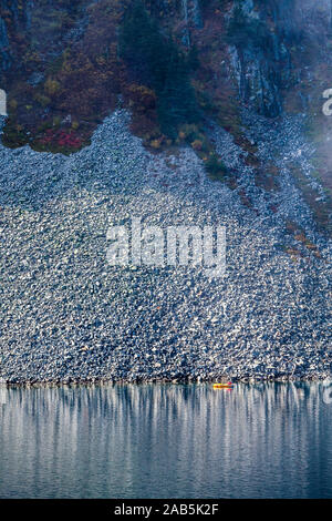 Un homme dans un petit radeau pneumatique de l'aviron sur le lac de la neige au-dessus de Snoqualmie Pass dans la partie centrale de la chaîne des Cascades dans l'État de Washington, USA. Banque D'Images