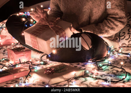 Femme de l'ouverture d'un cadeau de Noël sur le lit avec des lumières de Noël Banque D'Images