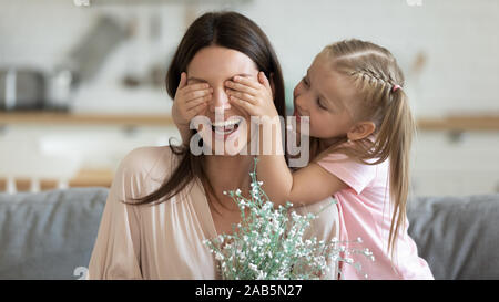 Enfant fille surprise faire fermer les yeux de maman présentant des fleurs Banque D'Images