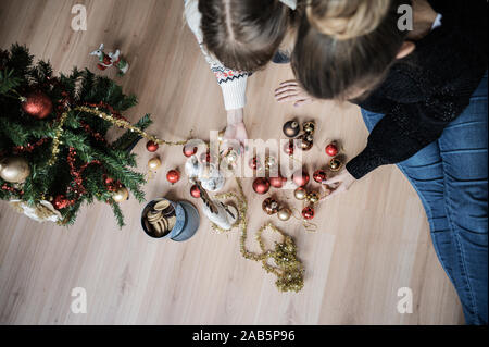 Vue supérieure de deux copines assis sur le plancher du salon de la décoration de Noël avec ruban brillant, babioles et une boîte de cookies sur le sol autour de t Banque D'Images