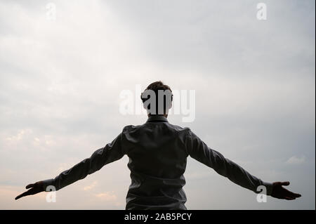 Vue de derrière d'un businessman standing sous ciel nuageux avec ses bras ouverts. Banque D'Images