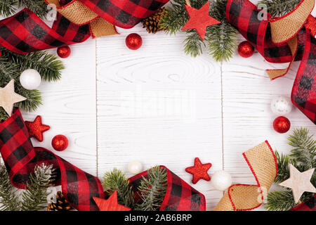 Cadre de Noël d'ornements, de branches, de jute et rouge et noir buffalo plaid ruban. Vue de dessus sur un fond de bois blanc. Banque D'Images