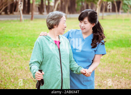 Smiling nurse helping senior woman de marcher autour du parc Banque D'Images