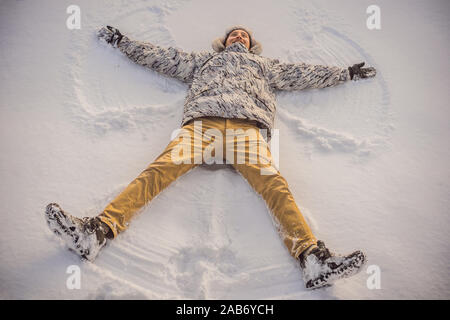 Un jeune homme en veste se trouve sur la neige et rend la figure d'un ange. Plaisir d'hiver Banque D'Images