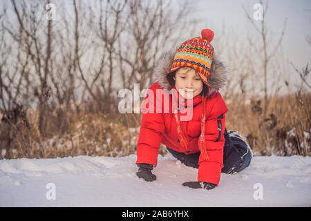 Vêtements mode garçon en rouge jouent à l'extérieur. Loisirs actifs avec enfants en hiver par temps froid. Garçon s'amusant avec la première neige. Happy little kid est Banque D'Images