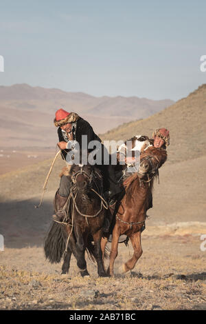 Les chasseurs eagle kazakhs prenant part à un match de lutte traditionnelle. Deux lutteurs à cheval commencer tirant sur une peau de mouton, celui qui le récupère, je Banque D'Images